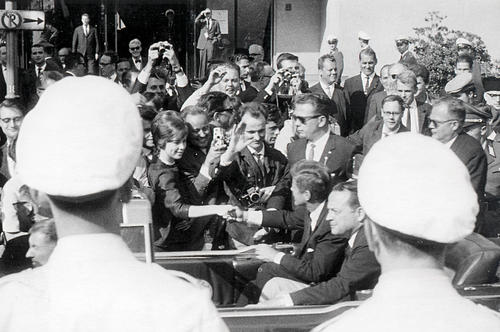 Im Blitzlichtgewitter: Eine junge Frau wird von Kennedy begrüßt, im Vordergrund ein Polizist, rechts hinten Berlins Regierender Bürgermeister Willy Brandt.
