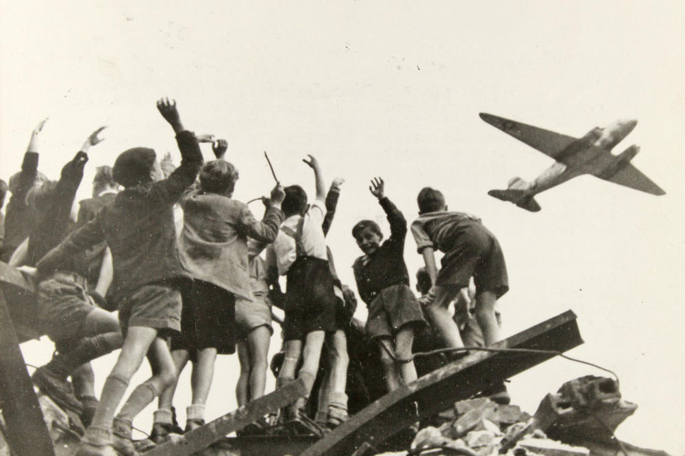 Rettung aus der Luft: Kinder winken im Juli 1948 einem „Rosinenbomber“ zu. Mit der Luftbrücke versorgten die Westalliierten während der Berlin-Blockade die Bevölkerung mit Lebensmitteln und lebenswichtigen Dingen wie Brennmaterial.
