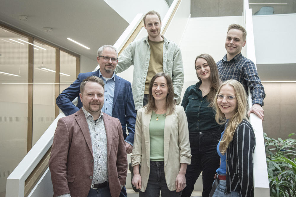 Gruppenbild der sieben Teammitglieder von MucosaTec auf der Treppe im Forschungsgebäude SupraFAB