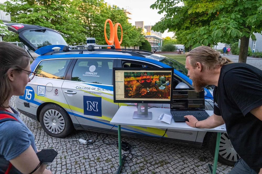 Auf einem Laptop-Bildschirm sehen, was das autonome Auto „sieht“: die umliegenden Gebäude, die Straßen und die Bewegungen der Menschen.