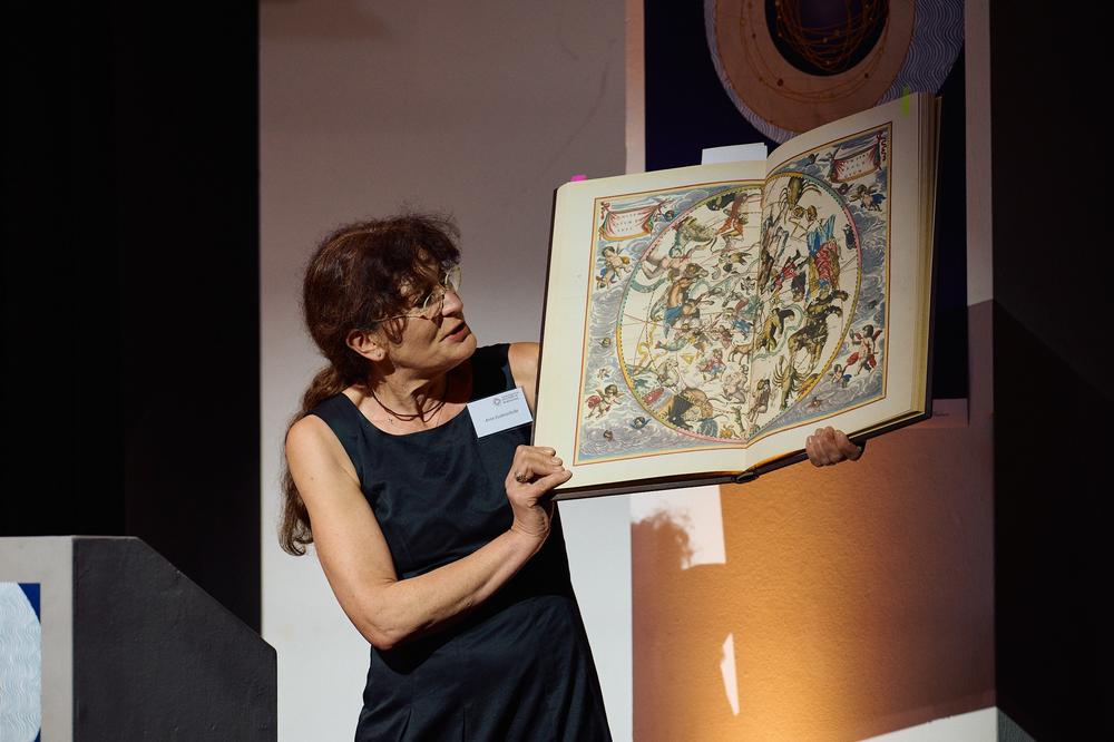 Professorin Anne Eusterschulte bei der Abschlusstagung im Juni 2024. Sie zeigt eine Faksimile-Ausgabe des Himmelsatlas Harmonia Macrocosmia des Astronomen, Mathematikers und Kartografen Andreas Cellarius (um 1596–1665).