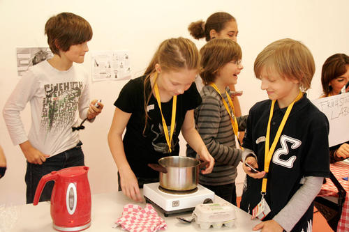 Anhand einer Stoppuhr messen die Kinder den Wattverbrauch der Küchengeräte nach