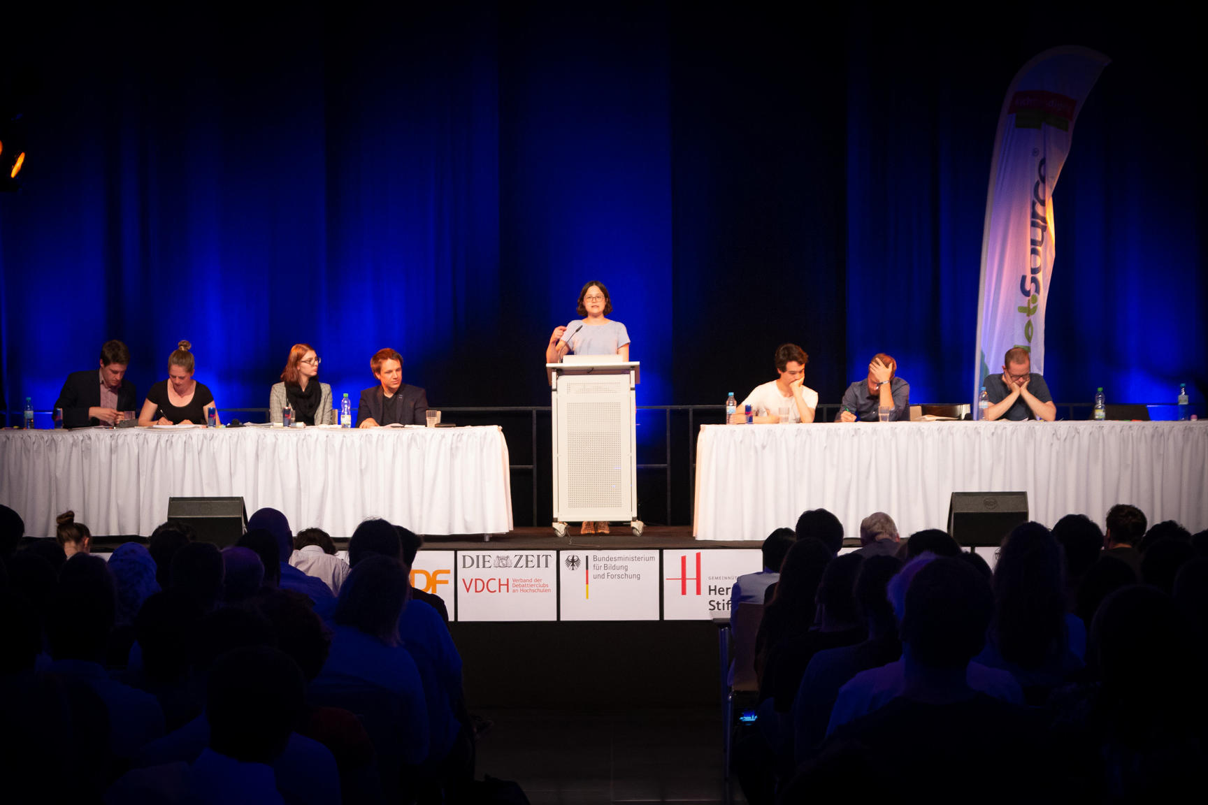 Endspurt zum Wettstreit um den Vizemeistertitel: Die Studentin der Literaturwissenschaft Lara Tarbuk hält ihre Rede im Finale der Debattiermeisterschaft. Rechts sitzen ihre Teamkameraden, links Studierende aus Heidelberg und Münster.