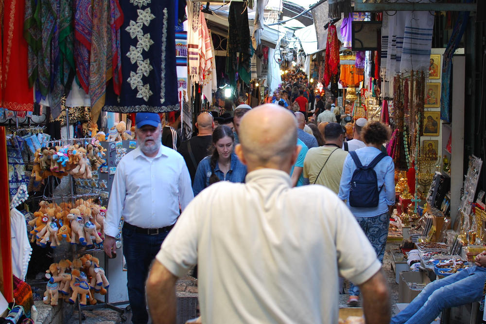 Ein Mann versucht einen Karren voll Brot durch die Gassen der Jerusalemer Altstadt zu schieben, die überfüllt sind mit Touristen, Gläubigen, überall sind kleine Läden.