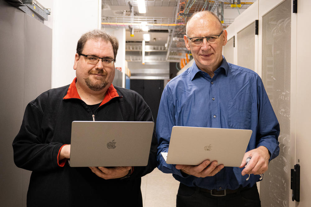 Johannes Posel, neuer Sicherheitsbeauftragter, und Dietmar Dräger, ehemaliger Sicherheitsbeauftragter, im Serverraum mit Laptops in der Hand