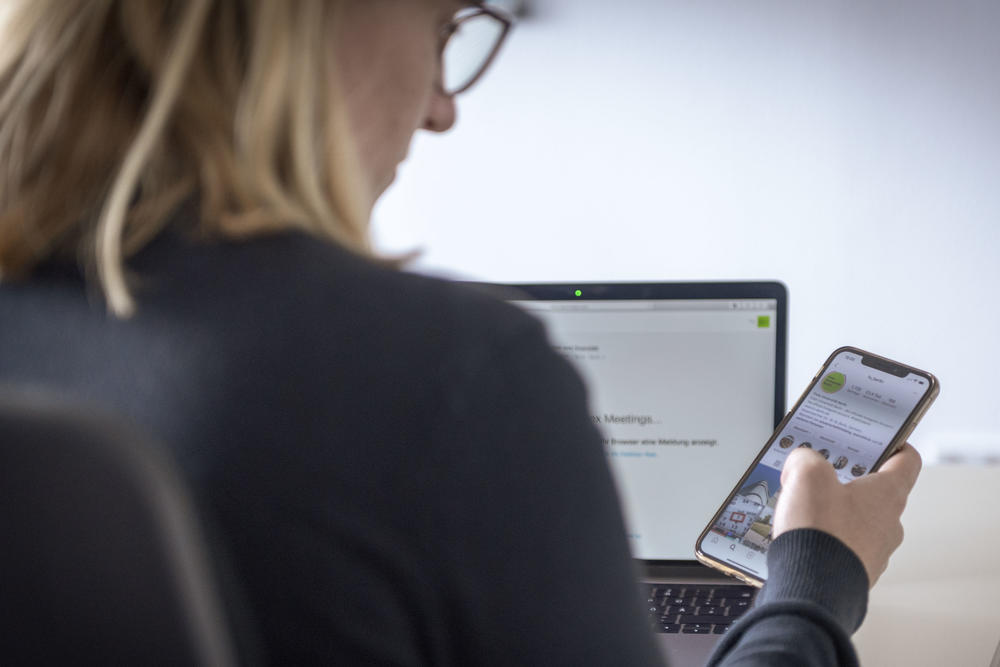 A woman is shown busy working with her smart phone and her laptop.