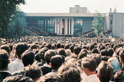 From the back of the crowd, President Kennedy is hardly visible, but his words can be clearly heard by all.