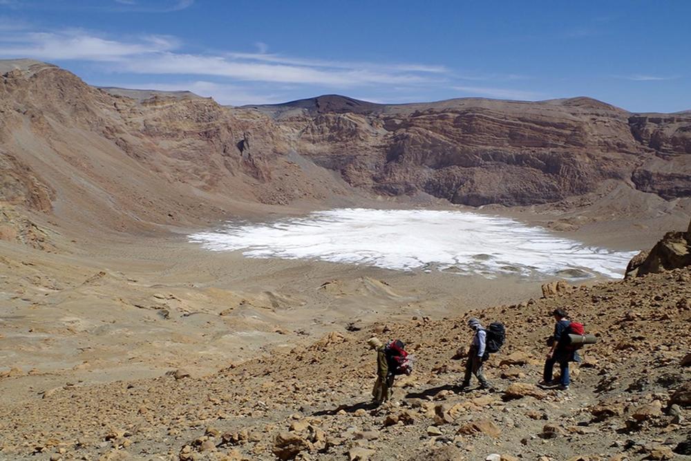 Abstieg in den Era-Kohor-Subkrater innerhalb der Gipfelcaldera des Emi Koussi - mit 3415 m der höchste Berg der Sahara. Auf dem Kraterboden liegen weißliche Sedimente: evaporitische Salzkrusten, Reste eines Paläosees, der den Krater teilweise füllte.