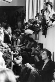 1. Volksuni vom 23. - 26.5.1980 an der FU. Die Volksuni ist den Kräften der Arbeit, der kritischen Wissenschaft, der Frauenbewegung, den Grünen, der Studentenbewegung und der alternativen Kultur gewidmet.Studenten im überfüllten Hörsaal.